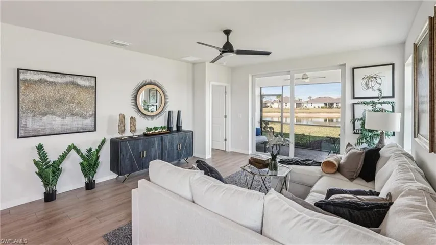 Expansive open concept living area featuring wood-finish flooring, a contemporary ceiling fan, and large sliding glass doors leading to an outdoor screened patio
