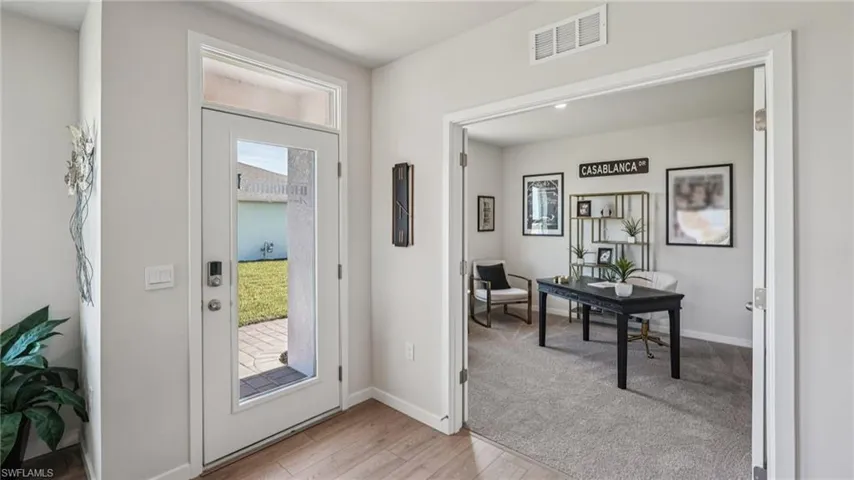 Entryway featuring a glass-paneled door with transom window, wood-finish flooring, and an adjacent room with carpeted flooring and double-door entry