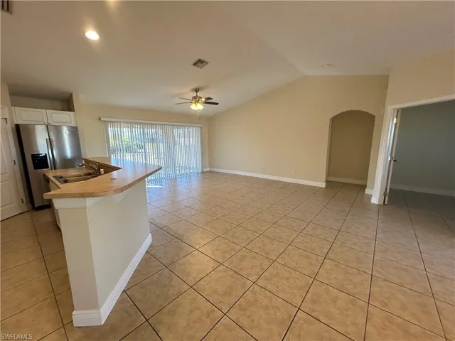 Kitchen featuring stainless steel refrigerator with ice dispenser, light countertops, vaulted ceiling, arched walkways, and light tile patterned floors