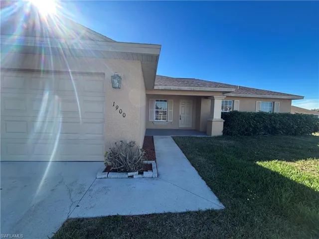 Property entrance with stucco siding, a yard, covered porch, and an attached garage