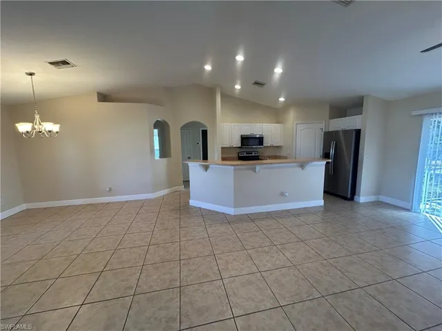 Kitchen featuring a kitchen breakfast bar, lofted ceiling, appliances with stainless steel finishes, arched walkways, and white cabinets