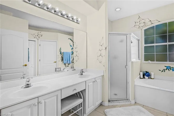 Dual vanity with integrated sinks, large mirror, walk-in shower with frosted glass, and a built-in soaking tub