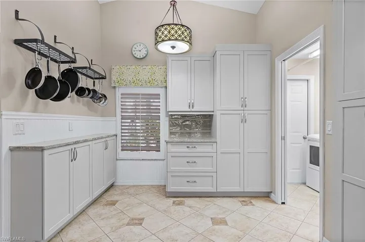 Kitchen with light stone countertops, light tile patterned floors, vaulted ceiling, and hanging light fixtures