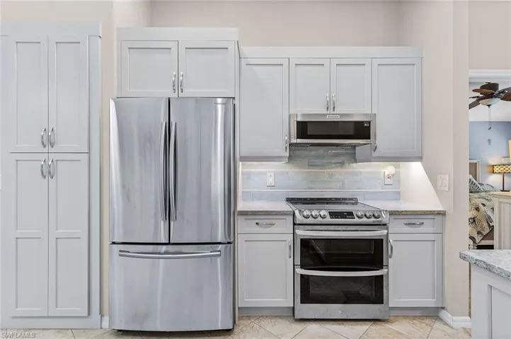 Kitchen with ceiling fan, light stone countertops, white cabinetry, stainless steel appliances, and tasteful backsplash