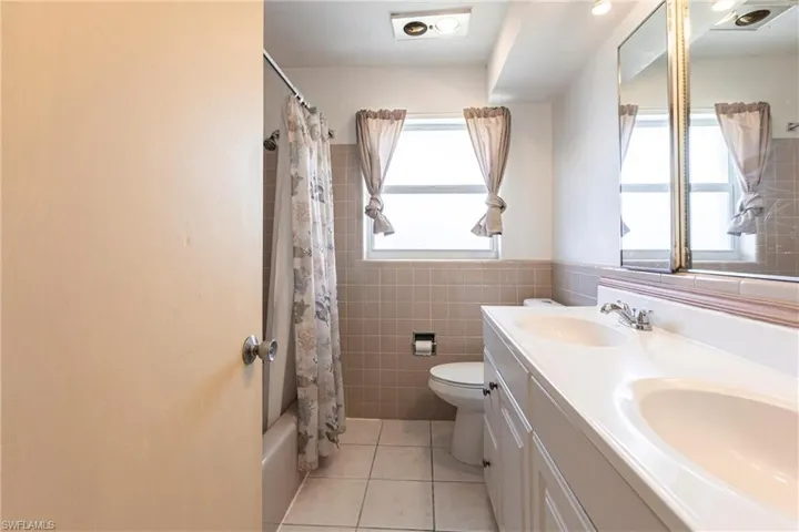 Bathroom featuring toilet, tile patterned floors, double vanity, tile walls, and shower / bathtub combination with curtain