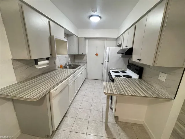 Kitchen featuring tasteful backsplash, white appliances, light tile patterned floors, under cabinet range hood, and light countertops