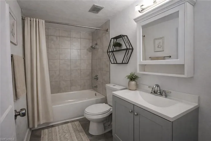 Full bath with vanity, shower / bathtub combination with curtain, and a textured wall