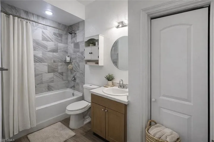 Full bath with vanity, shower / bath combo with shower curtain, and dark wood-type flooring
