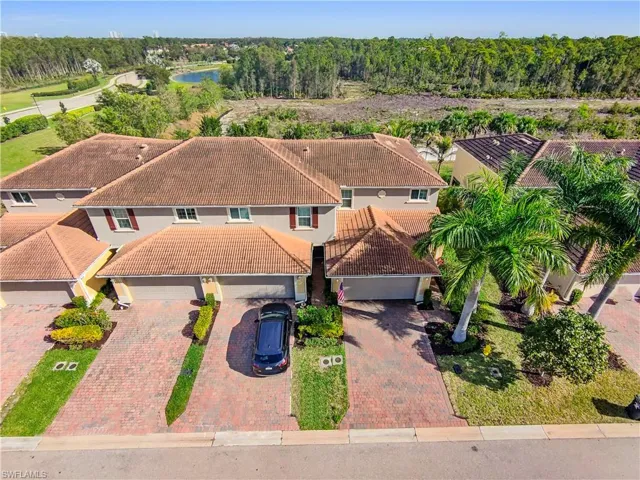 Townhome property featuring a tile roof, brick paver driveway, attached garage, and mature palm trees