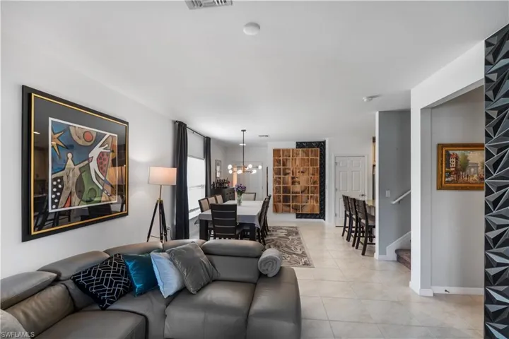 Open-concept interior featuring light-toned tile flooring, a dining area with a linear pendant light fixture, a breakfast bar with seating, a white paneled door, and a staircase with a white handrail