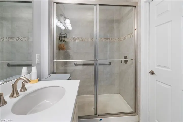 Bathroom featuring a glass-enclosed shower with tile surround, decorative mosaic accent band, and integrated grab bars