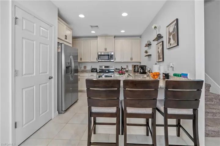 Kitchen featuring light cabinetry, stainless steel appliances, recessed lighting, a breakfast bar with stone-finish countertop, and tile flooring