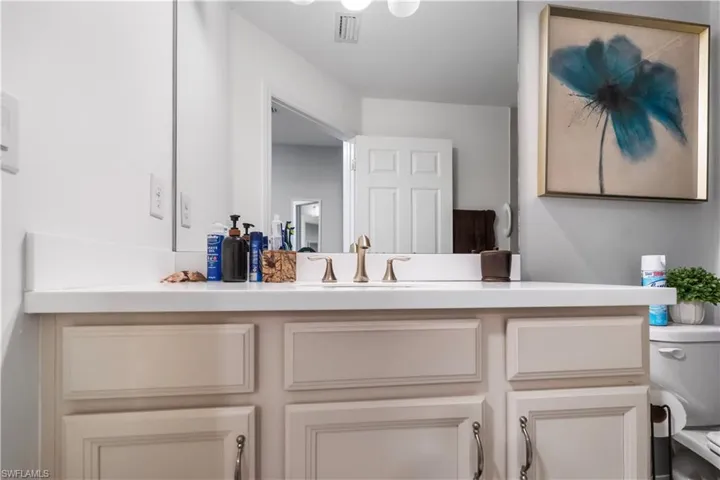 Vanity with a white countertop and integrated sink, bronze-finish faucet, and light-toned cabinetry with dark hardware