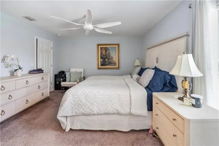 Carpeted bedroom featuring a ceiling fan with integrated lighting, light blue wall paint, a white paneled door, and a curtained window