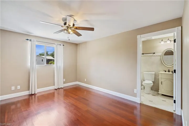 Unfurnished bedroom with baseboards, wood finished floors, ceiling fan, and ensuite bathroom
