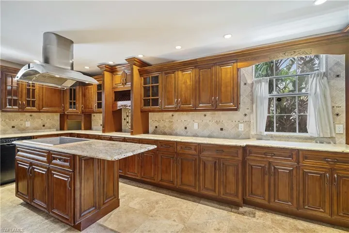 Kitchen featuring granite counters, backsplash, glass insert cabinets, island range hood, and stainless appliances