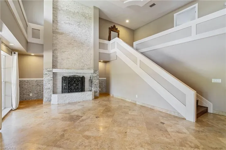 Unfurnished living room featuring stairs, a high ceiling, and a brick fireplace