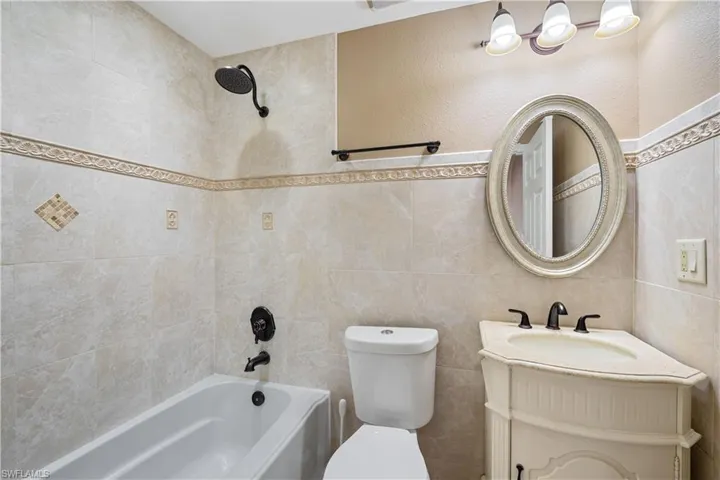 Full ensuite bath with tile walls, toilet, vanity, and bathing tub / shower combination