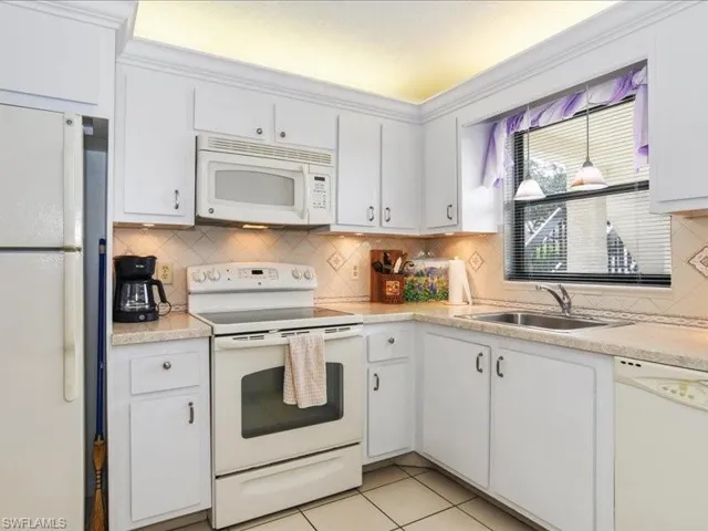 Kitchen with light tile patterned flooring, white appliances, white cabinetry, and sink