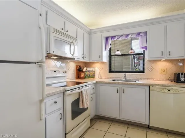 Kitchen with white cabinetry, sink, light tile patterned floors, and white appliances