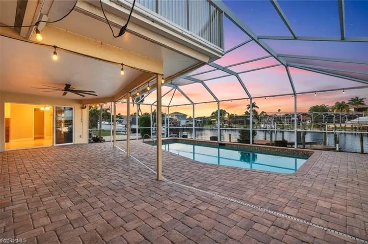 Pool at dusk featuring a patio area, a sunroom, an outdoor pool, and glass enclosure