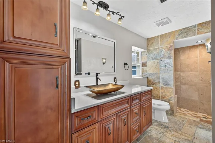 Bathroom with wood cabinetry, vanity, a tile shower, and stone tile flooring
