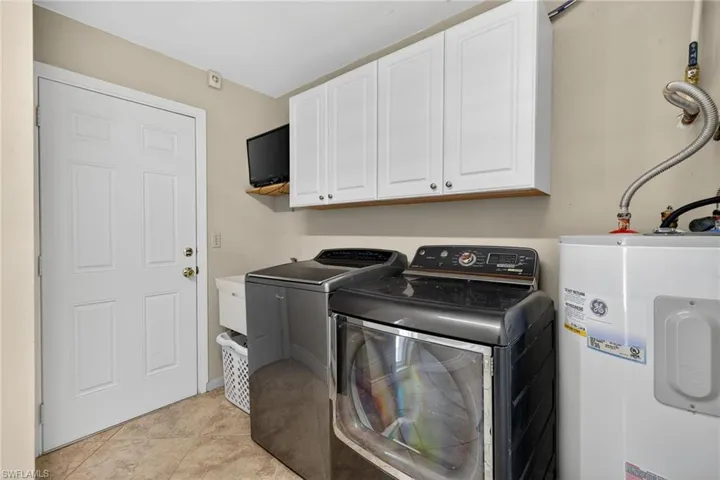 Laundry room with water heater, cabinet space, washing machine and dryer, and light tile patterned floors