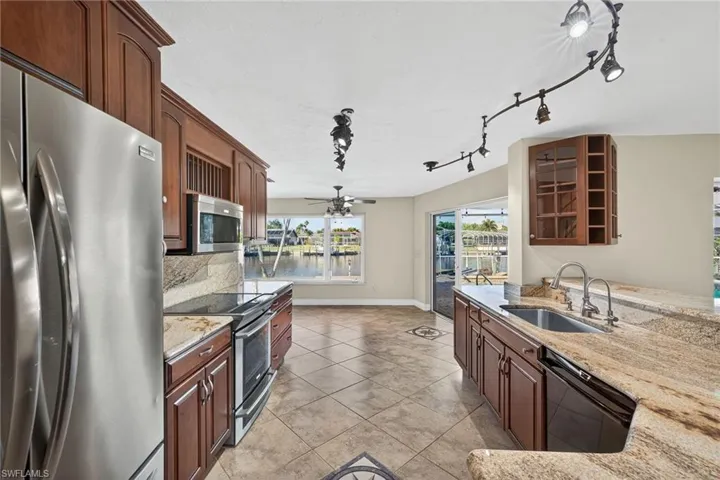 Kitchen with Electrolux appliances with stainless steel finishes, light stone countertops, track lighting, a ceiling fan, and light tile patterned floors