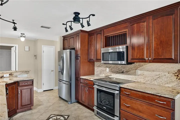 Kitchen with appliances with stainless steel finishes, light stone countertops, tasteful backsplash, light tile patterned flooring, and pendant lighting