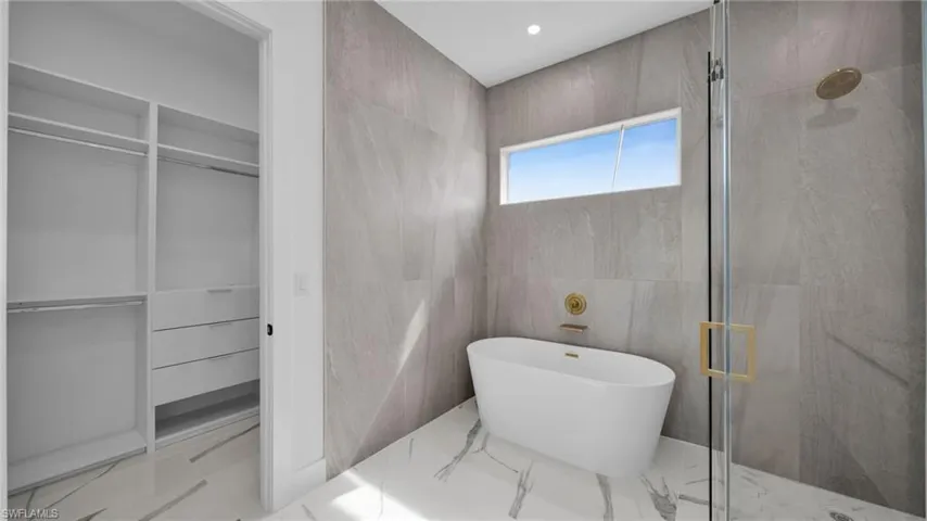 Bathroom with tile walls, a stall shower, a freestanding tub, light marble finish floors, and a spacious closet