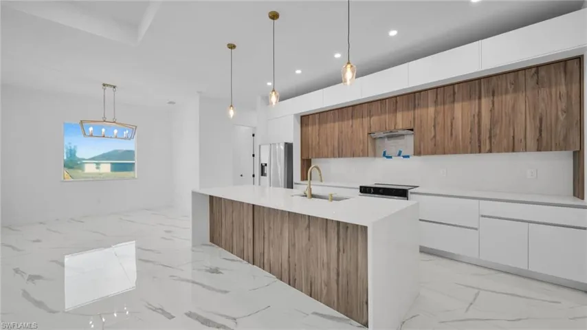 Two tone kitchen with modern cabinets, decorative light fixtures, two tone color scheme, light stone countertops, and light marble finish flooring