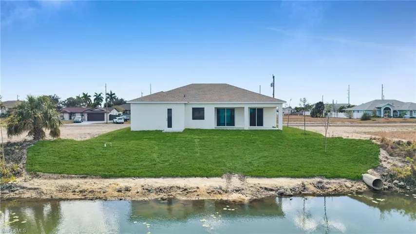 Rear view of house featuring stucco siding, a water view, a yard, and a patio area