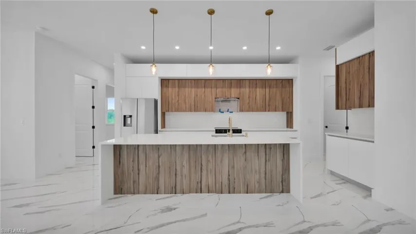 Kitchen featuring an island with sink, modern cabinets, light stone countertops, two tone cabinetry, and stainless steel fridge