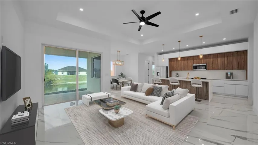 Living room with a ceiling fan, a raised ceiling, light marble finish flooring, and a chandelier virtual staged