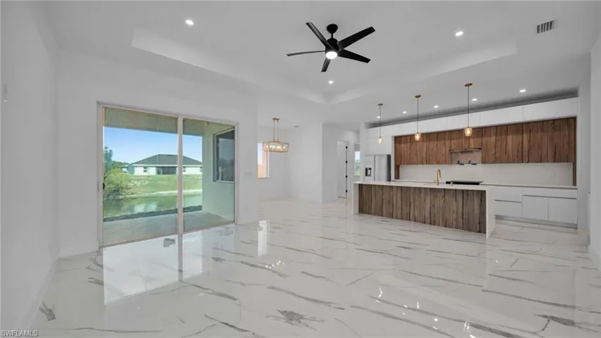 Unfurnished living room featuring a ceiling fan, a raised ceiling, light marble finish flooring, and recessed lighting