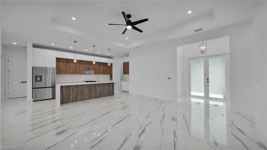 Unfurnished living room featuring a ceiling fan, light marble finish floors, recessed lighting, a tray ceiling, and french doors
