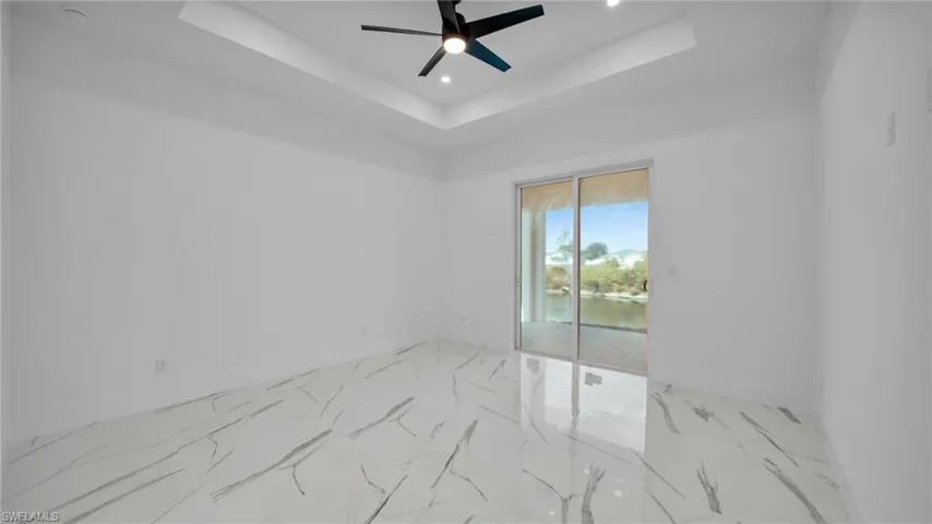 Empty room with ceiling fan, a raised ceiling, recessed lighting, a water view, and light marble finish floors