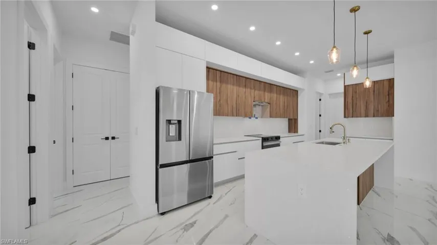 Dual tone kitchen featuring modern cabinets, decorative light fixtures, stainless steel fridge with ice dispenser, light stone countertops, and two tone cabinetry