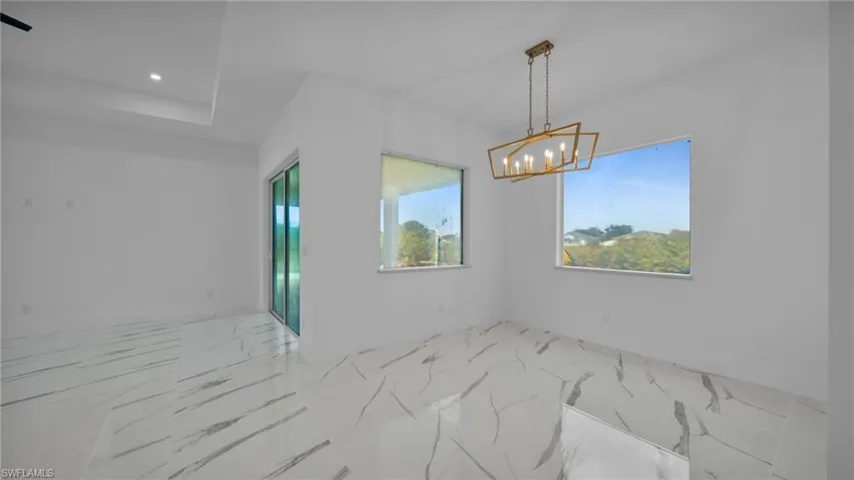 Empty room featuring suspended lighting, plenty of natural light, and light marble finish floors
