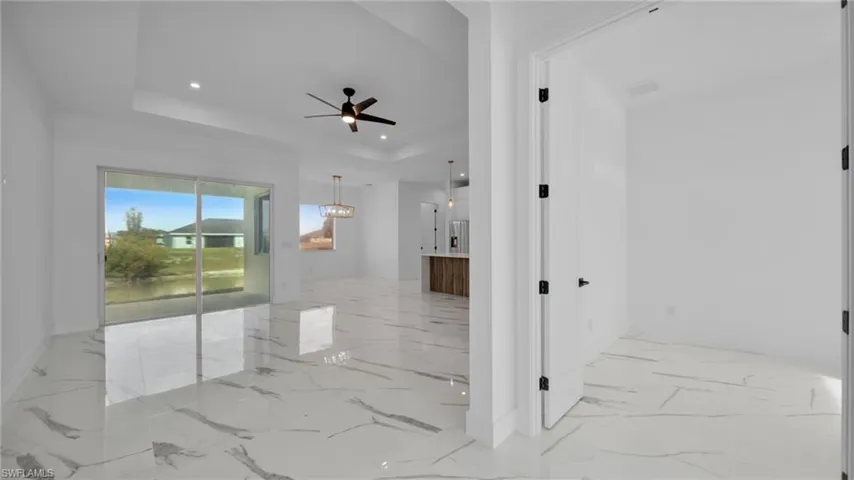 Empty room featuring a tray ceiling, recessed lighting, ceiling fan, and light marble finish floors