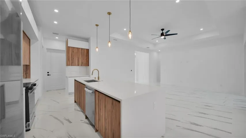 Two tone kitchen with modern cabinets, an island with sink, hanging light fixtures, light stone countertops, and stainless steel appliances