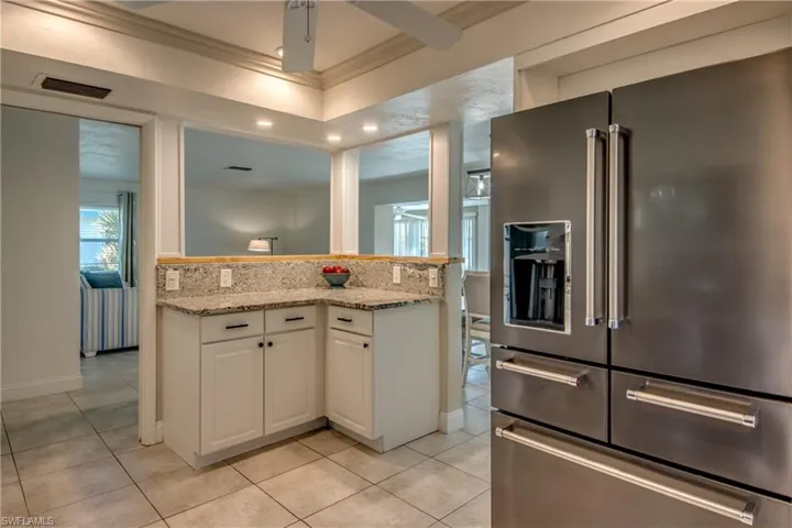 Kitchen with high end fridge, ornamental molding, light tile patterned flooring, white cabinets, and light stone countertops
