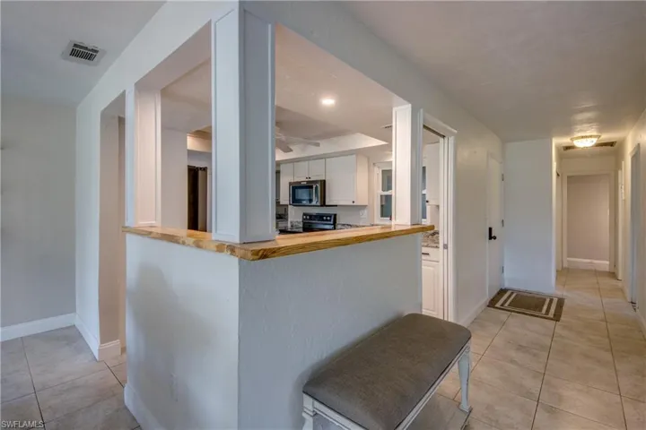 Kitchen with electric range, stainless steel microwave, light tile patterned floors, butcher block counters, and white cabinetry