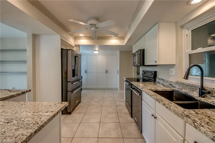 Kitchen with stainless steel appliances, crown molding, a raised ceiling, a ceiling fan, and white cabinetry