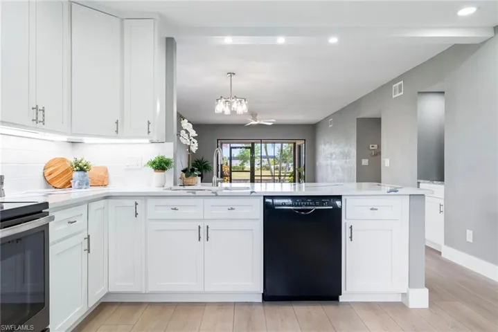 White shaker cabinetry, light-toned wood-finish flooring, white subway tile backsplash, recessed lighting, and a kitchen island with a built-in dishwasher