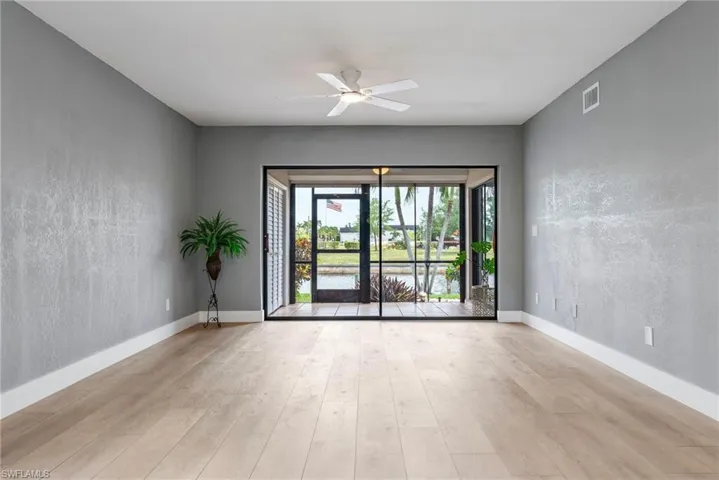 Wood-finish flooring throughout, ceiling fan with integrated lighting, and sliding glass doors opening to an outdoor area with water frontage