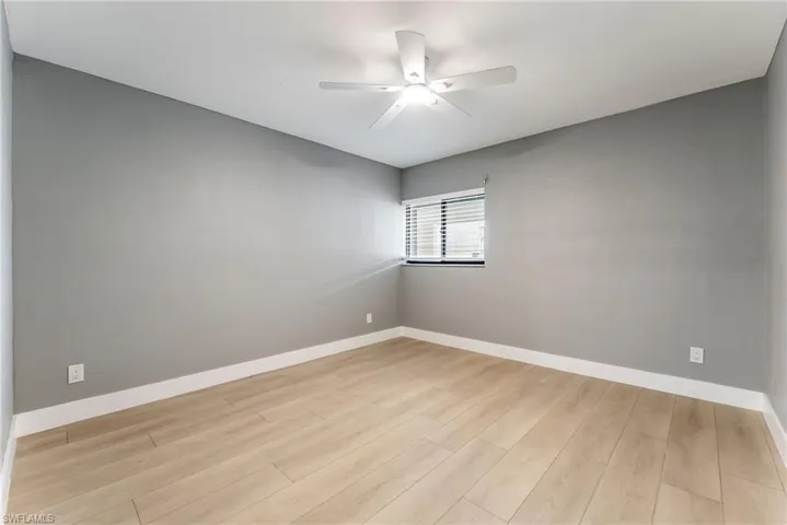 Light wood-finish flooring, neutral gray walls, and a ceiling fan with integrated lighting