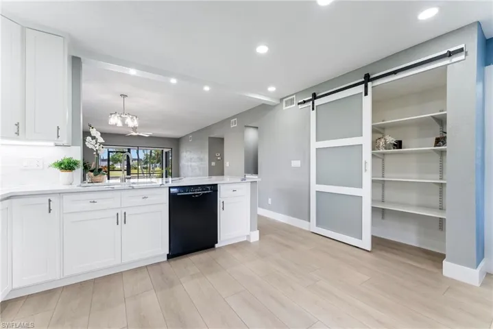 White shaker cabinetry, light wood-finish flooring, recessed lighting, modern barn door, and a built-in shelving unit