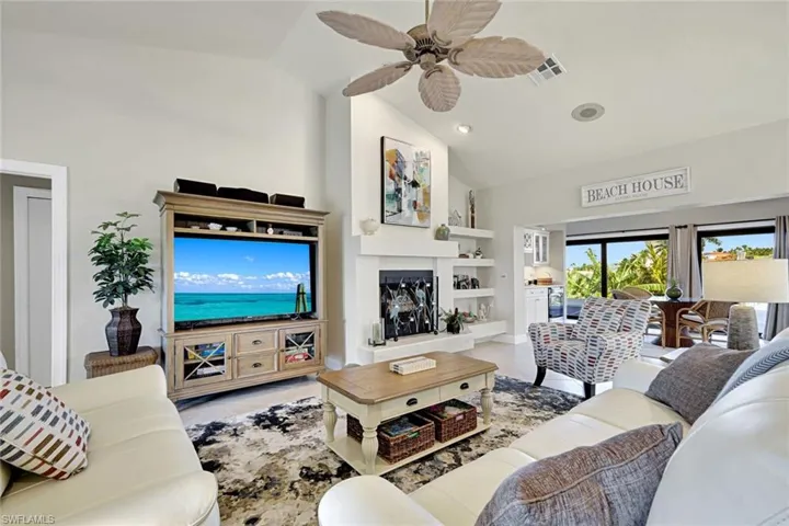 Tiled living room featuring ceiling fan, vaulted ceiling, recessed lighting, built in features, and a fireplace with raised hearth