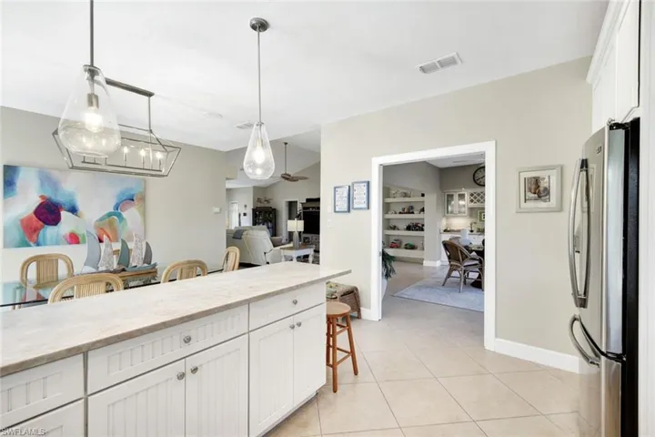 Kitchen featuring white cabinetry, a breakfast bar, freestanding refrigerator, hanging light fixtures, and light stone counters